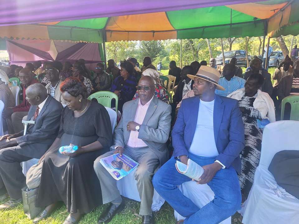 Long’ole seated at a public event, reading through documents