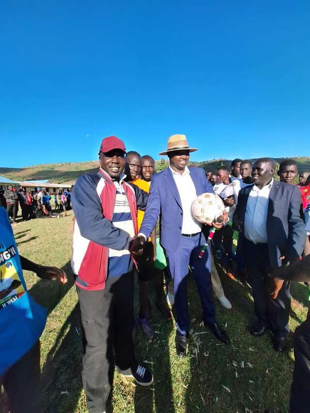 Long’ole holding a football and shaking hands with a supporter in front of young players